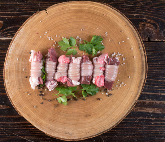 Torcinelli di Ovino su un piatto di legno, involtini di interiora di agnello con foglie di coriandolo.