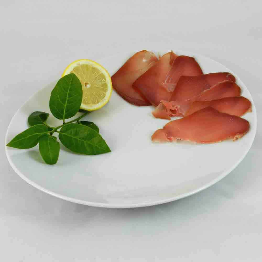 Bresaola di Tonno slices arranged on a plate with lemon and leaves for garnish.