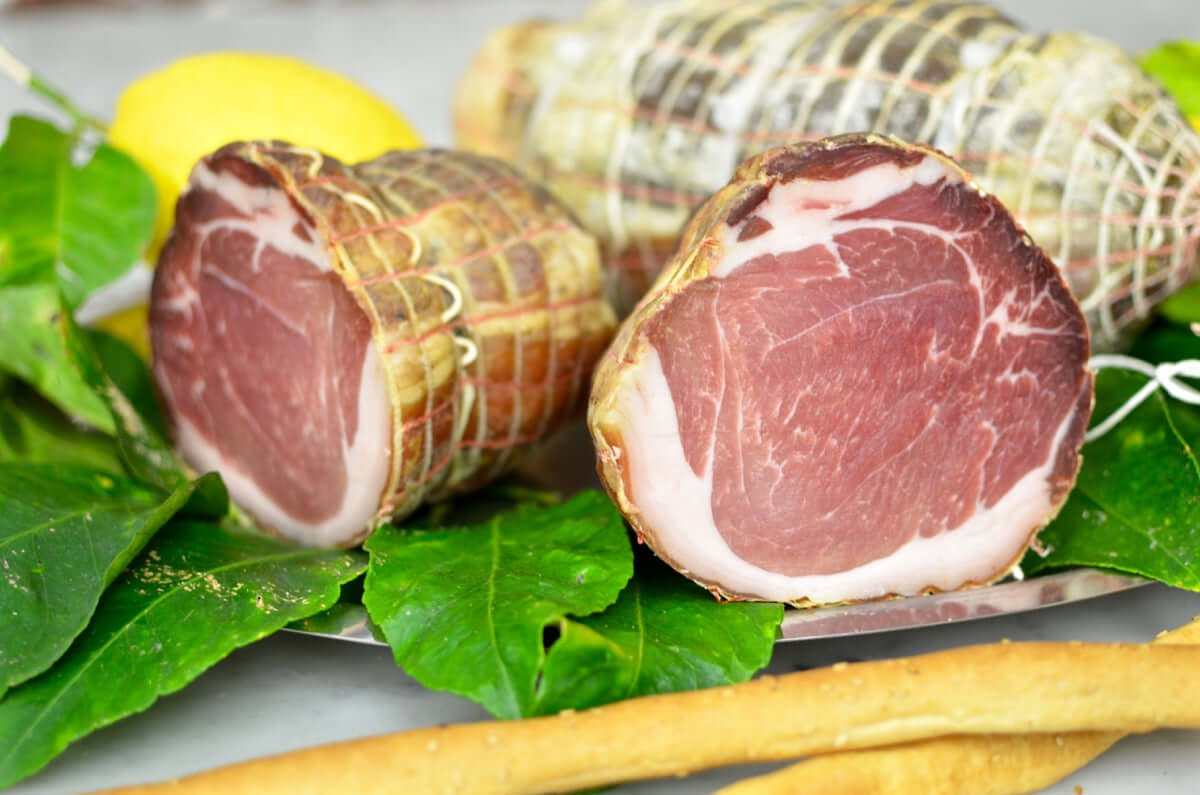 Capocollo Reale di Maiale Brado, un salume rustico e tradizionale, servito su un piatto con foglie fresche.