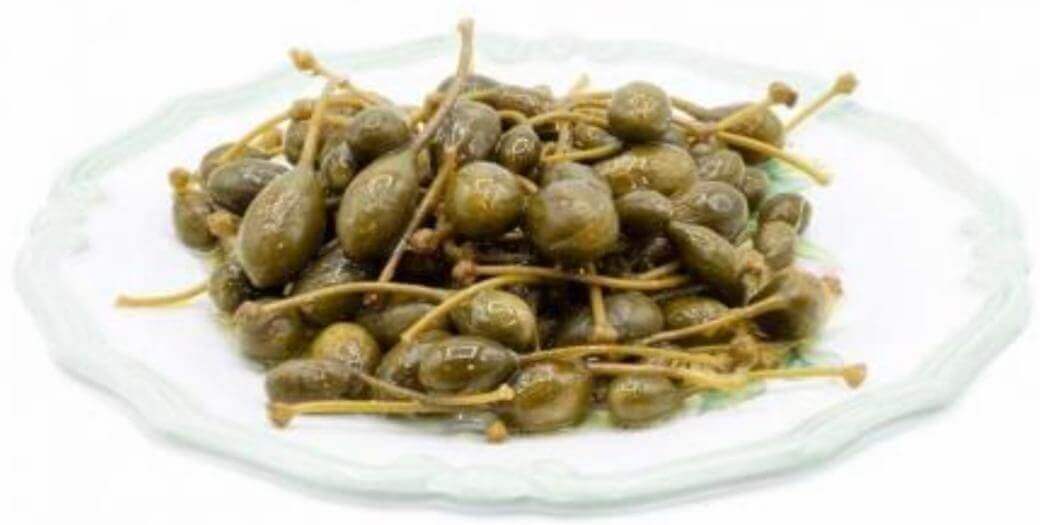 Capperi con gambo in aceto di vino su un piatto, condimento versatile per piatti e antipasti.