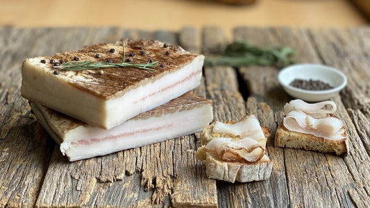 Lardo di Norcia Tradizionale stagionato alle erbette aromatiche su tavola di legno con pane e pepe nero.