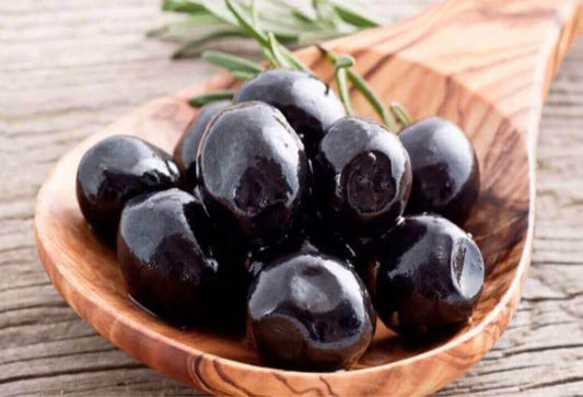 Olive Nere Giants in a wooden spoon, showcasing their rich flavor and dark color, perfect for gourmet recipes.