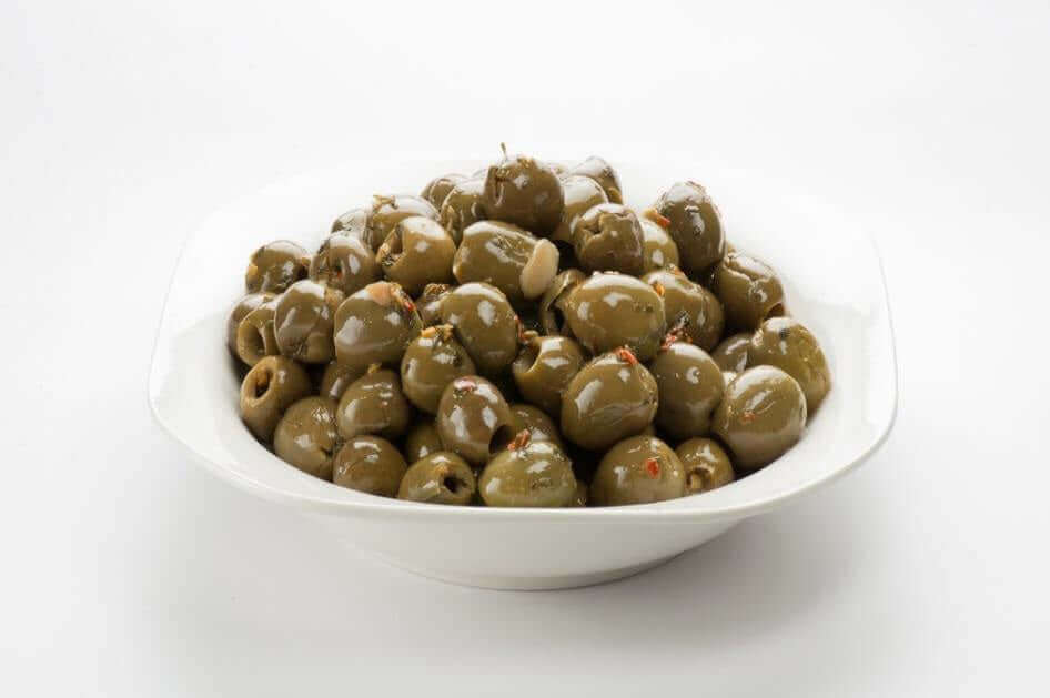 Olive verdi grandi denocciolate in olio di girasole served in a white bowl, garnished with spices.
