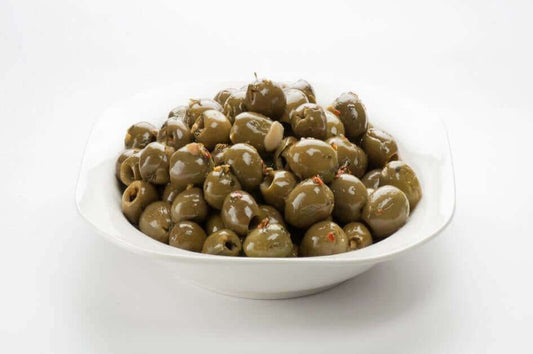 Olive verdi grandi denocciolate in olio di girasole served in a white bowl, garnished with spices.