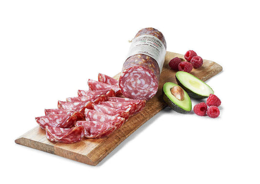 Salame Napoli affettato su un tagliere di legno con avocado e lamponi freschi.