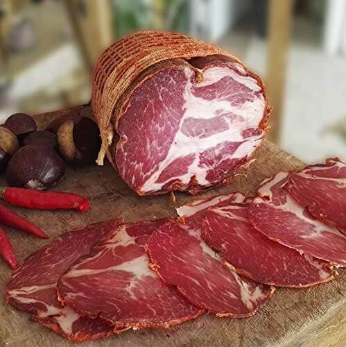 Capocollo - Artigianal, cured meat with slices on a wooden board, featuring chili peppers and nuts.