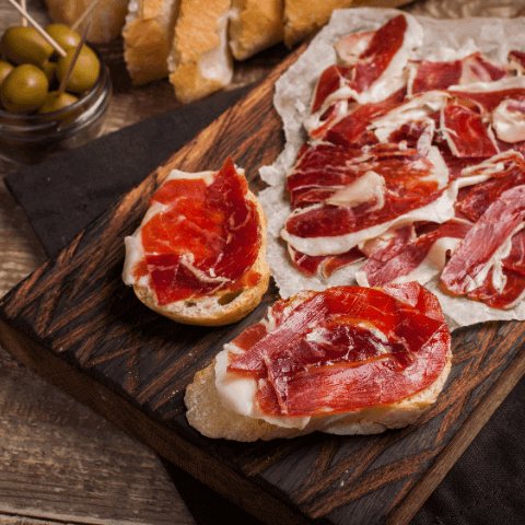 Spanish tapas with serrano ham, bread slices, and green olives on a rustic wooden board