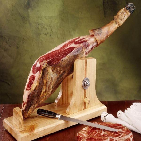 Traditional Spanish ham leg on wooden stand with carving knife on table, ready for slicing and serving.