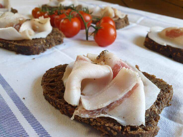 Delicious Lardo Arrotolato served on dark bread with fresh cherry tomatoes, showcasing artisanal Italian cuisine.