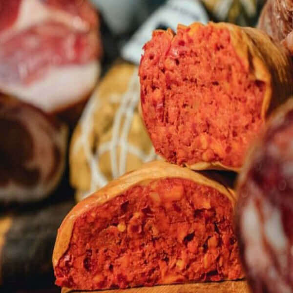 Nduja di Spilinga cut in artisanal casing showcasing bright red color and texture with natural smoking.