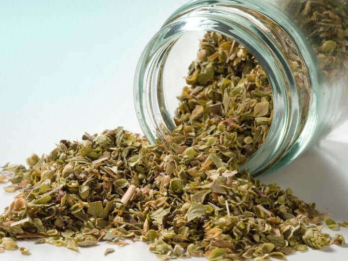 Origano a mazzetto in un barattolo di vetro, con foglie aromatiche sparse.