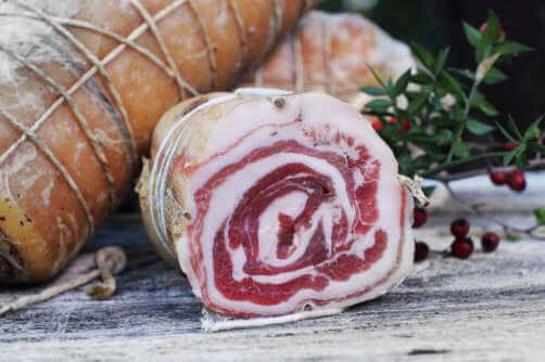 Pancetta Arrotolata, fetta di pancetta con striature di carne e grasso, presentata su un tavolo rustico.