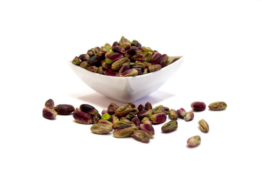 Pistacchio Sicilia - intero, sgusciato in ciotola bianca con pistacchi sparsi.