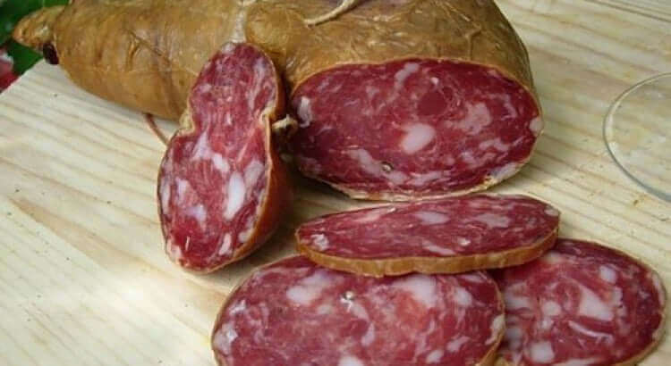 Soppressata Grecanica Calabrese sliced and whole, showcasing its rich colors and textures on a wooden board.