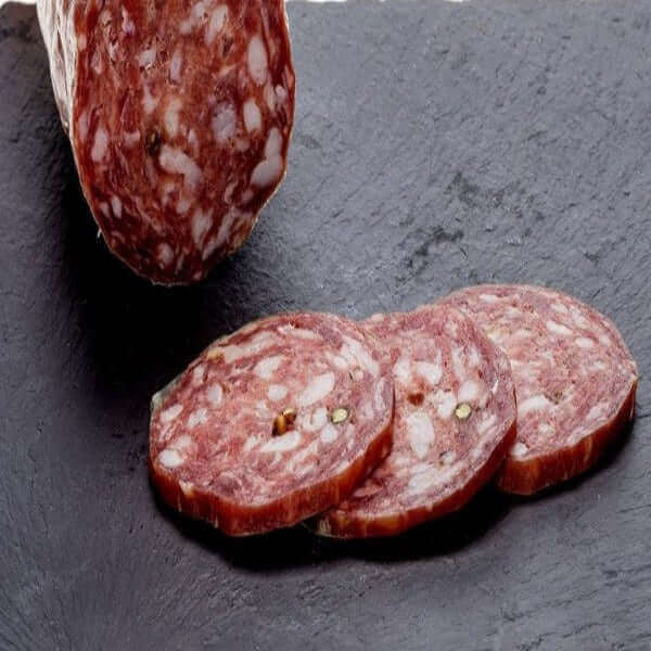 Salame Napoli slices on slate with artisanal whole salami in background, showcasing its rich red color and texture.