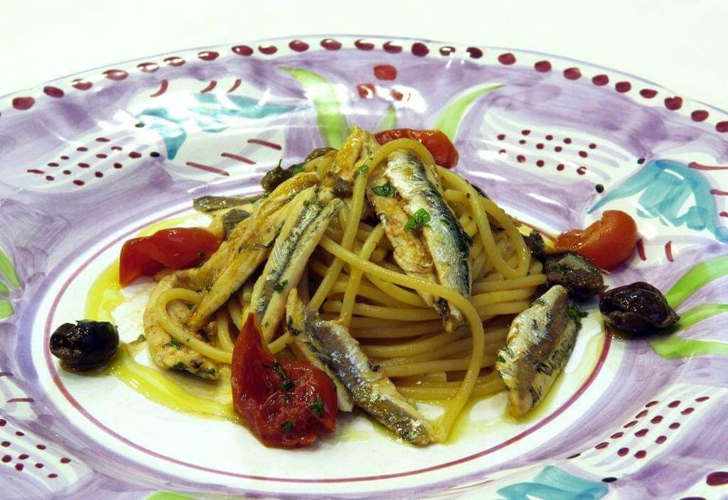 Delicious pasta dish with Colatura di Alici, topped with anchovies, cherry tomatoes, and olives on a decorative plate.