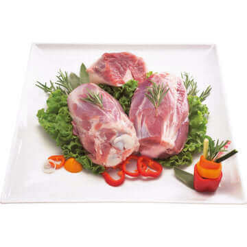 Stinco Crudo di Maiale Ner displayed on a white platter with fresh greens and vegetables.