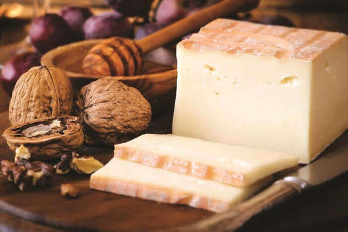 Taleggio DOP cheese displayed with walnuts and honey on a wooden platter, showcasing its creamy texture and washed rind.