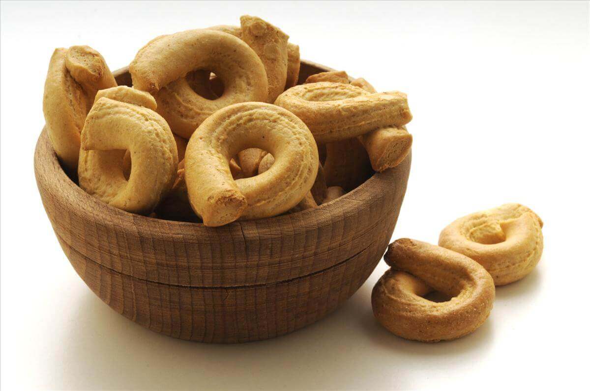 Bowl of golden-brown ring-shaped savory biscuits on a white background.