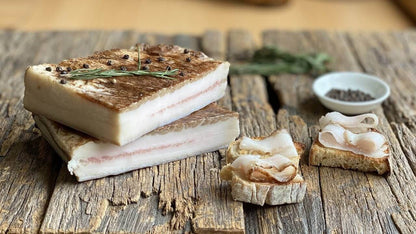 Lardo di Norcia Tradizionale stagionato alle erbette aromatiche su tavola di legno con pane e pepe nero.