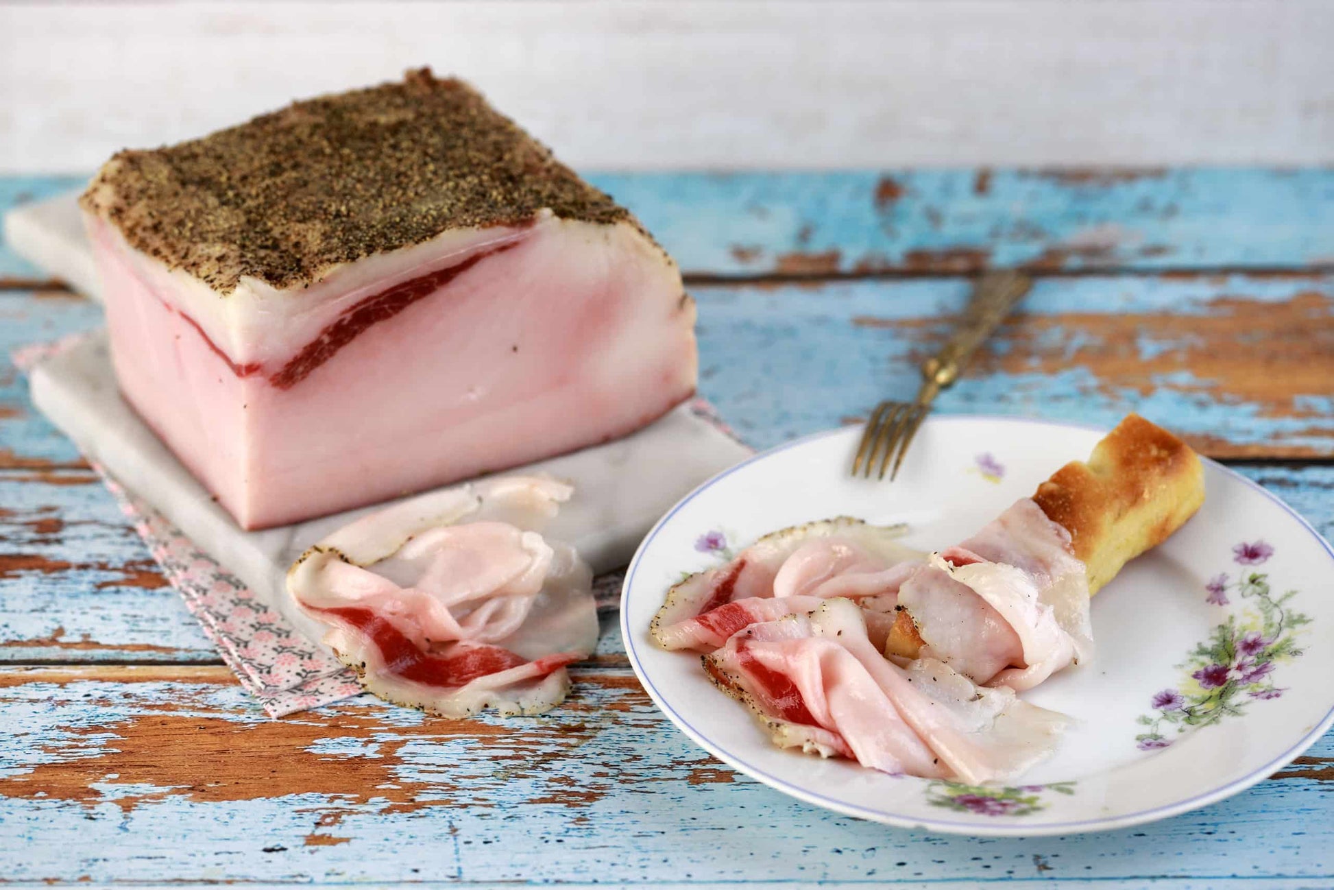 Sliced Lardo di Patanegra stagionato in CONCA on a decorated plate with a fork and bread on a rustic wooden table