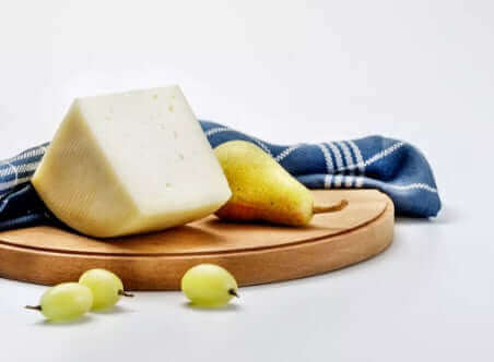 Pecorino Sardo Dop cheese wedge on wooden board with pear, grapes, and blue cloth in background