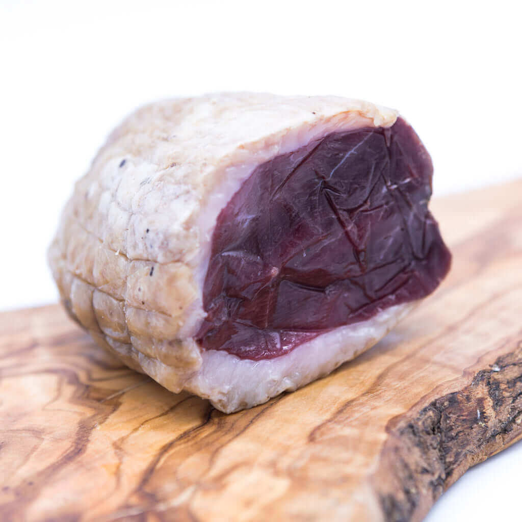 Stagionato petto d'oca affumicato da 500 gr, tagliato su tagliere in legno.