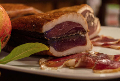 Sliced Petto D’Oca Stagionato on a white platter showcasing rich flavor and slightly smoked texture for gourmet charcuterie boards.