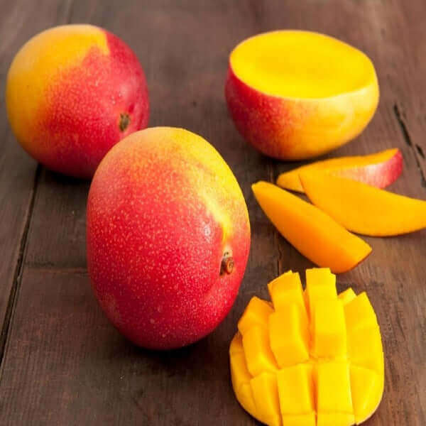 Fresh whole and sliced mangoes on a wooden table.