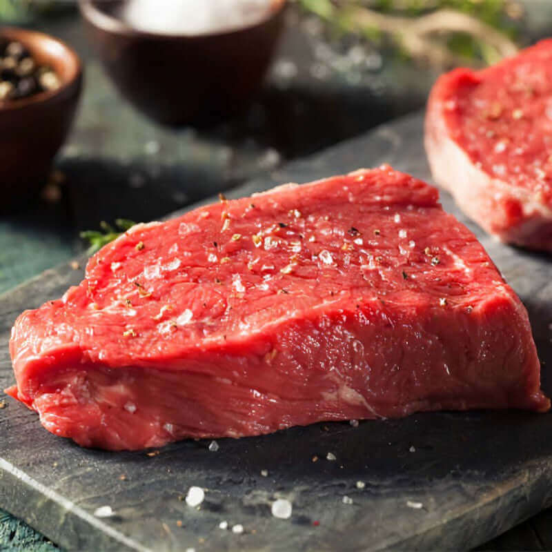 Fresh raw beef steak seasoned with salt and pepper on a cutting board